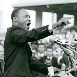 Dr. King speaks emphatically before a crowd, arm outstretched for emphasis.