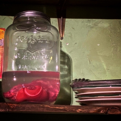 A jar with a pink, pickled pig's foot inside. There is a stack of plates next to the jar.