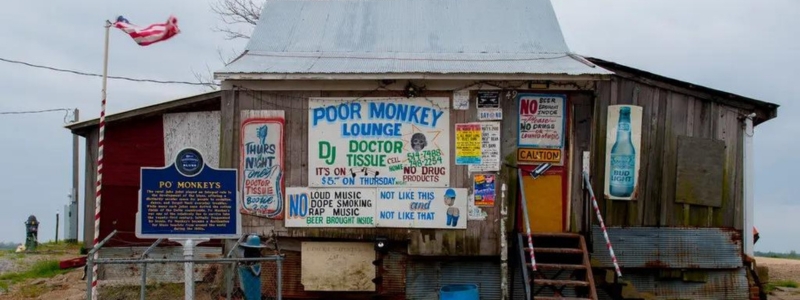 A small, wooden shack with a tin roof. There is a sign that says "Poor Monkey Lounge" and lots of colorful advertisements on the outside of the building.