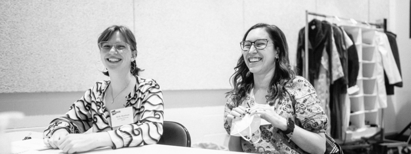 Two people seated together. They are laughing.