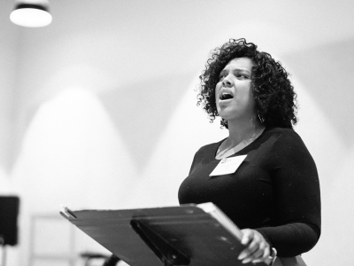 A person sings standing behind a raised music stand.