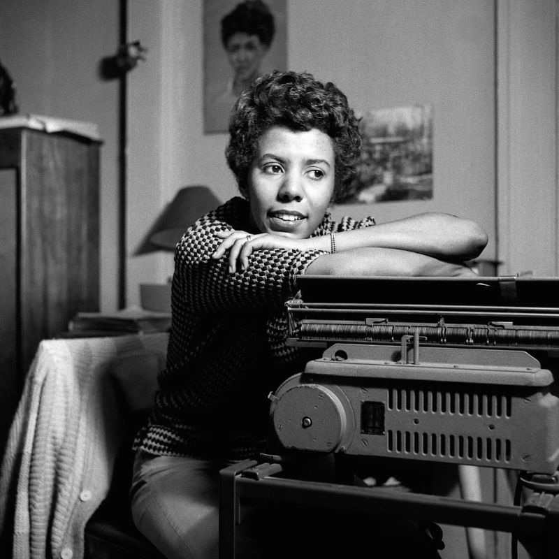 Lorraine Hansberry rests her chin on her arms, which are crossed over a typewriter.