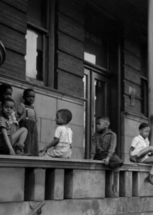 Nine young Black children sit talking and laughing near and on the stone stoop of an apartment building, Chicago 1941.