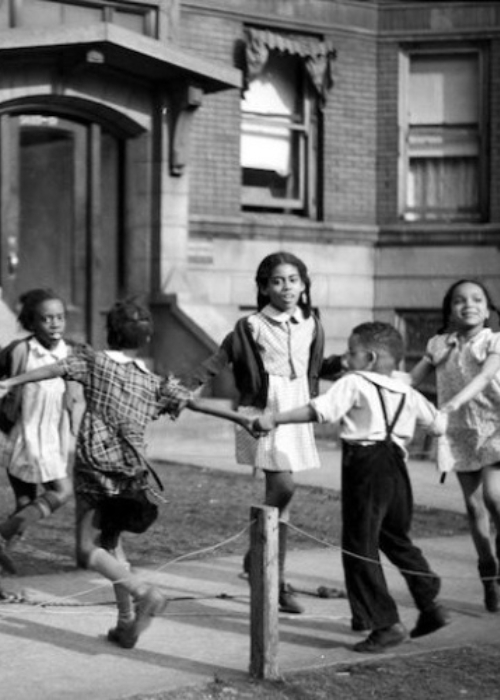 Eight young Black children hold hands and skip in a circle in front of an apartment building, Chicago 1941.